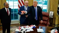 Presiden AS, Donald Trump menyodorkan kartu merah yang diberikan presiden FIFA, Gianni Infantino ke arah jurnalis yang meliput pertemuan mereka di Oval Office Gedung Putih pada Selasa (28/8). (AP/Evan Vucci)