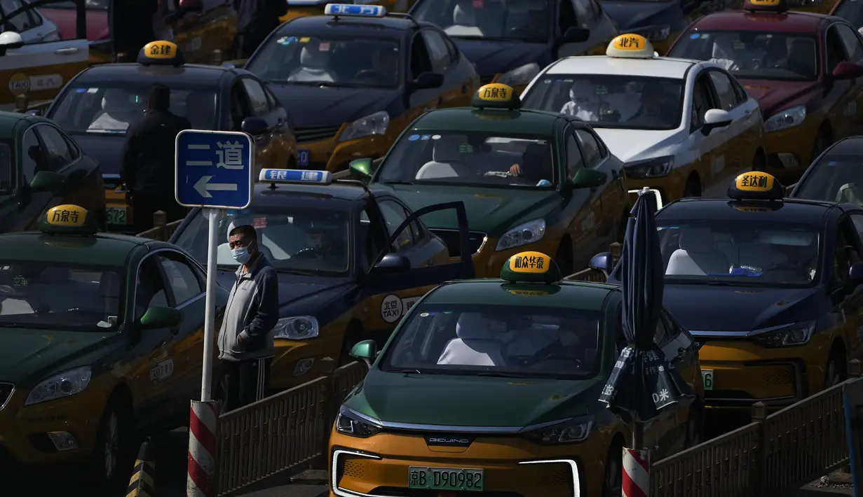 Seorang sopir taksi yang mengenakan masker berdiri menonton ketika mereka menumpuk untuk menunggu pelanggan di stasiun kereta api di Beijing, Kamis (6/10/2022). Xinjiang yang luas adalah wilayah China terbaru yang terkena pembatasan perjalanan COVID-19, karena China semakin meningkatkan langkah-langkah pengendalian menjelang kongres penting Partai Komunis akhir bulan ini. (AP Photo/Andy Wong)