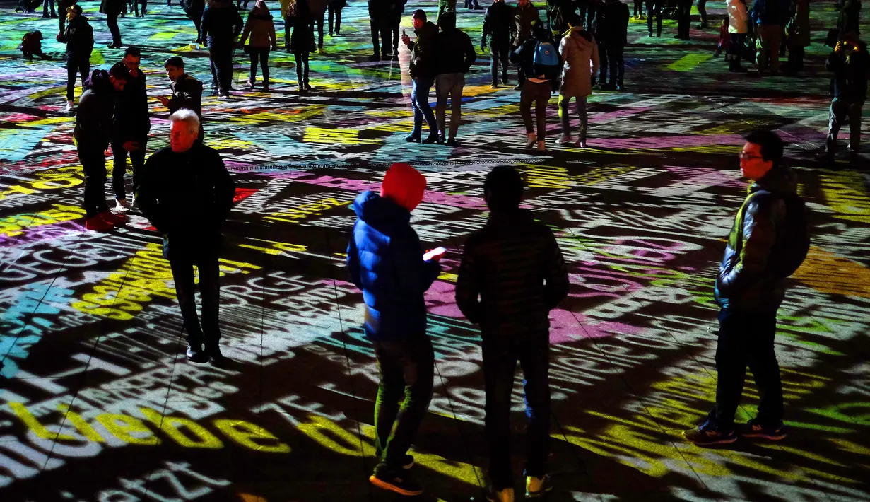 Sejumlah pengunjung bercincang di tengah lapangan yang dihiasi instalasi cahaya di depan gedung Katedral Cologne, Jerman (31/12). Mereka merayakan tahun baru dengan menikmati cahaya laser di Kota Cologne. (AFP/Patrik Stollarz)