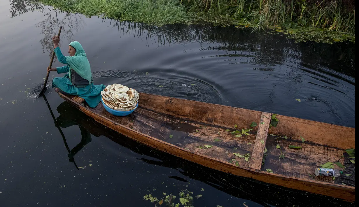 Seorang wanita Kashmir berjualan roti segar mendayung kapalnya di Danau Dal di Srinagar, Kashmir yang dikuasai India (18/10/2020). (AP Photo/Dar Yasin)