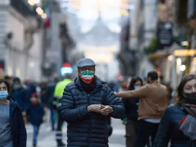 Seorang pejalan kaki, mengenakan masker dengan bendera Italia di atasnya, berdiri di jalan Roma, Kamis (23/12/2021). Pemerintah Italia telah mewajibkan kembali penggunaan masker di luar ruangan untuk menahan peningkatan kasus Covid-19 yang didorong oleh varian Omicron. (Filippo MONTEFORTE/AFP)