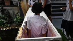 Seorang siswa remaja mencoba masuk ke dalam peti mati di Kid Mai Death Awareness Cafe, Thailand (30/3). Cafe ini menyediakan ruang pameran yang dibangun untuk mendidik masyarakat tentang kematian dan agama Buddha di Bangkok. (AFP/Lillian Suwanrumpha)