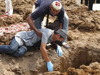 Seorang pria jatuh ke tanah saat dia menangis selama pemakaman kerabat yang meninggal karena COVID-19 di TPU Rorotan, Jakarta, Rabu (7/7/2021). Indonesia menghadapi gelombang kedua COVID-19. (AP Photo/Tatan Syuflana)