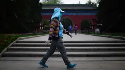 Seorang wanita mengenakan topi berjalan di taman di Beijing (19/4). Beijing memiliki populasi 21.150.000 pada tahun 2013. (AFP Photo/Wang Zhao)