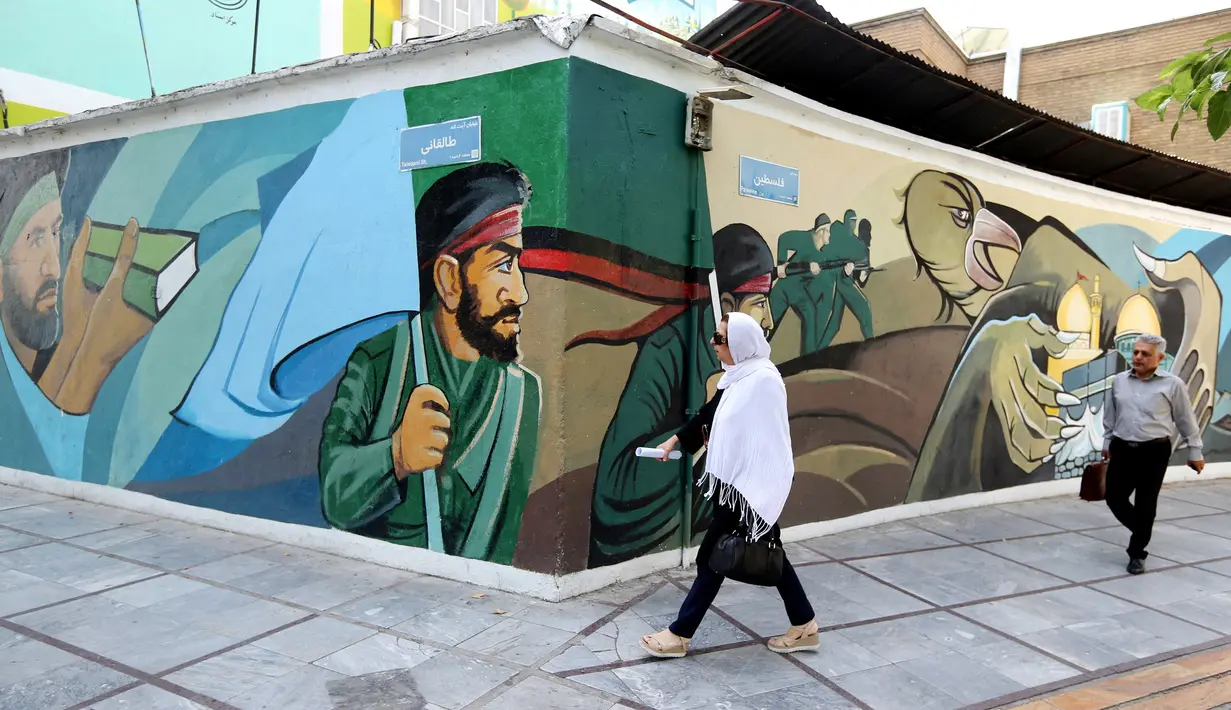 Pejalan kaki melewati lukisan mural yang menggambarkan para prajurit Iran di Palestine Square, Ibu Kota Teheran, Iran, Sabtu (22/6/2019). (ATTA KENARE/AFP)