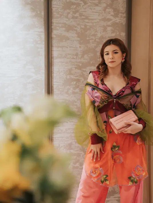 Shalom mengenakan sleeveless dress bernuansa floral dengan potongan v-neck yang rendah dipadukan dengan celana merah muda. Sebagai outer, ia mengenakan crop top tulle jacket berwarna hijau olive. (instagram/sharazaaa)