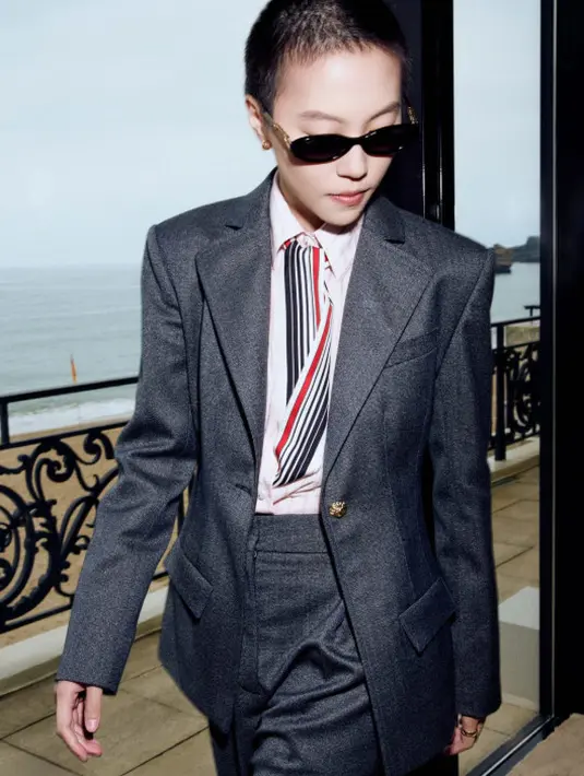 Leah Dou, brand ambassador Chanel, mengenakan jaket wol mouline warna charcoal yang dipadukan dengan celana senada serta kemeja pin berbahan katun-sutra berwarna pink pucat, Look 4 dari koleksi pre-collection Fall-Winter 2026 Ready-to-Wear. Penampilannya dilengkapi dengan aksesori, tas, dan sepatu dari Chanel, serta sentuhan riasan dari Chanel Makeup. (Foto: Chanel.dok)