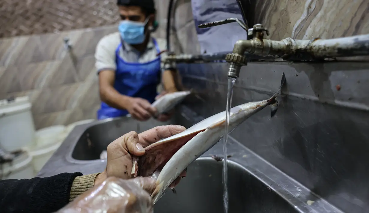 Pemuda Palestina mencuci ikan kembung sebelum diasapi untuk dijual di pasar ikan menjelang liburan Idul Fitri di kota Rafah di Jalur Gaza selatan (3/5/2021). Ikan makarel yang diolah melalui metode pengasapan ini merupakan hasil tangkapan nelayan Palestina melaut. (AFP/Said Khatib)