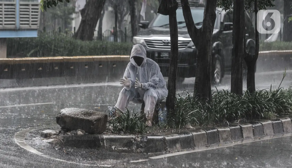 Tukang parkir mengenakan jas pelindung saat hujan mengguyur di Jalan Pramuka, Jakarta, Kamis (18/2/2021). BMKG mengimbau pengguna jalan agar berhati-hati saat berkendara karena musim hujan disertai angin kencang diprediksi terus berlanjut hingga akhir Februari. (merdeka.com/Iqbal S Nugroho)