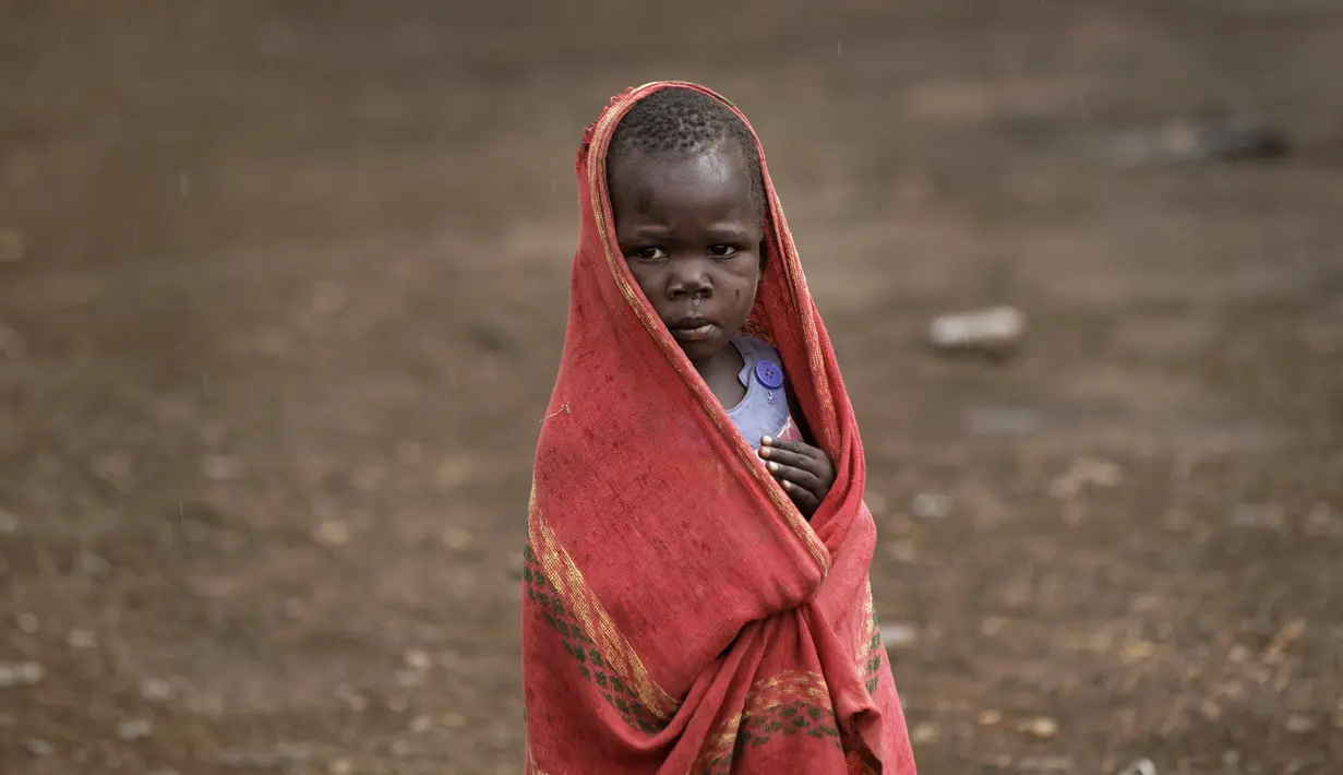 Seorang anak pengungsi muda Sudan Selatan berlindung dari rintik hujan di pemukiman pengungsi Bidi Bidi, Uganda, Selasa (6/6). Bidi Bidi adalah pemukiman pengungsi terbesar di dunia yang menampung pengungsi Sudan Selatan. (AP Photo / Ben Curtis)
