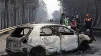 Polisi berdiri di dekat sebuah mobil yang terbakar di sebuah jalan antara Castanheira de Pera dan Figueiro dos Vinhos, Portugal tengah, 18 Juni 2017 (AFP)