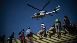 Sebuah helikopter terlihat saat para imigran memanjat pagar perbatasan antara Meksiko dan AS di Tijuana, Meksiko (25/11). Ratusan migran berusaha menyerbu pagar perbatasan yang memisahkan Meksiko dari AS. (AFP Photo/Pedro Pardo)