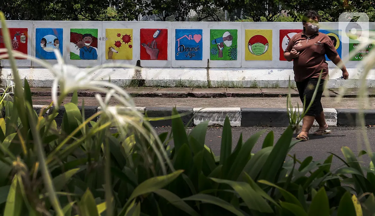 Warga melintasi mural sosialisasi bahaya COVID-19 di Jalan Sultan Iskandar Muda, Jakarta, Rabu (23/9/2020). PSBB pengetatan sepekan terakhir ini belum efektif menurunkan angka jumlah harian Covid-19 di DKI yang tercatat bertambah 1.122 kasus di ibu kota pada Selasa (22/9). (Liputan6.com/Johan Tallo)
