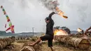 Seorang peserta menyalakan meriam yang terbuat dari batang pohon dengan menggunakan karbit dan air untuk menciptakan suara ledakan selama Festival Kuluwung, di Sukasirna, Jawa Barat, pada tanggal 5 April 2025. (ADITYA AJI/AFP)