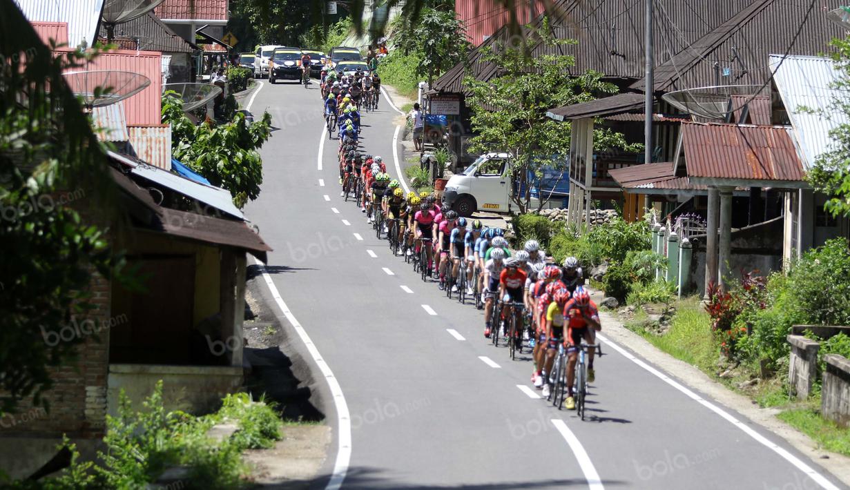 Pebalap melintasi perkampungan sepanjang etape ke-5 Tour de Singkarak dari Pantai Carocok-Painan menuju pantai Gondoriah-Pariaman, Sumatera Barart. (Bola.com/Nicklas Hanoatubun)