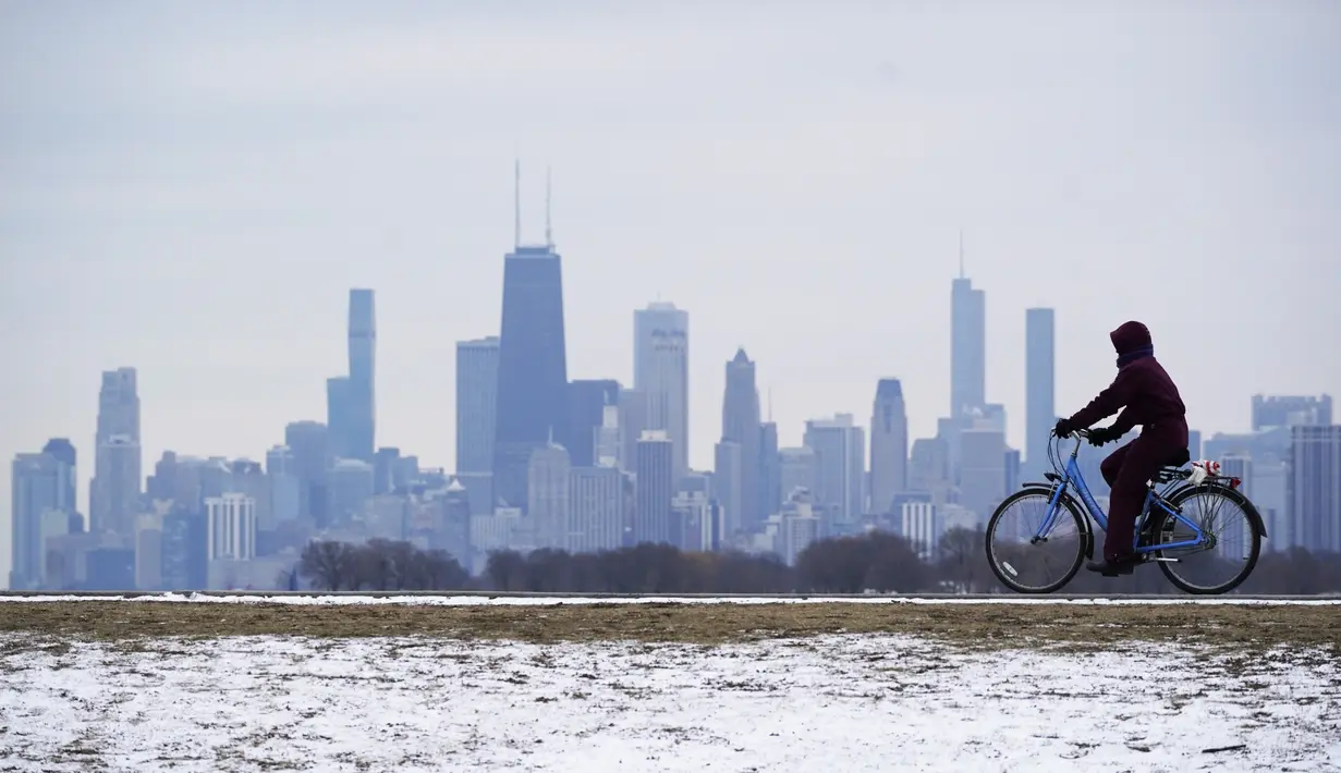 Seorang pria mengendarai sepedanya di dekat debu tipis salju di Pantai Montrose di Chicago (17/1/2022). Badai salju Chicago diperkirakan akan membawa hingga 5 inci di sepanjang Danau Michigan. (AP Photo/Nam Y. Huh)