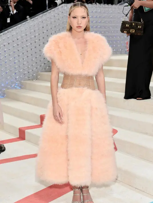 Menemani sang ibu, Lila Moss tampil feminin dengan puffy dress dari Fendi Couture. Gaun berbulu itu memiliki detail korset transparan yang memamerkan perut rata Lila Moss [@katemossagency]