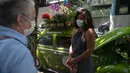 Roberta Machado (kanan) asal Brasil dan pelanggan berbincang di sebelah VW Beetle 1969 miliknya yang diubah menjadi toko bunga keliling di Copacabana, Rio de Janeiro, Rabu (14/10/2020). Perempuan 51 tahun ini mengubah VW kodok untuk bertahan dari krisis akibat pandemi COVID-19. (MAURO PIMENTEL/AFP)