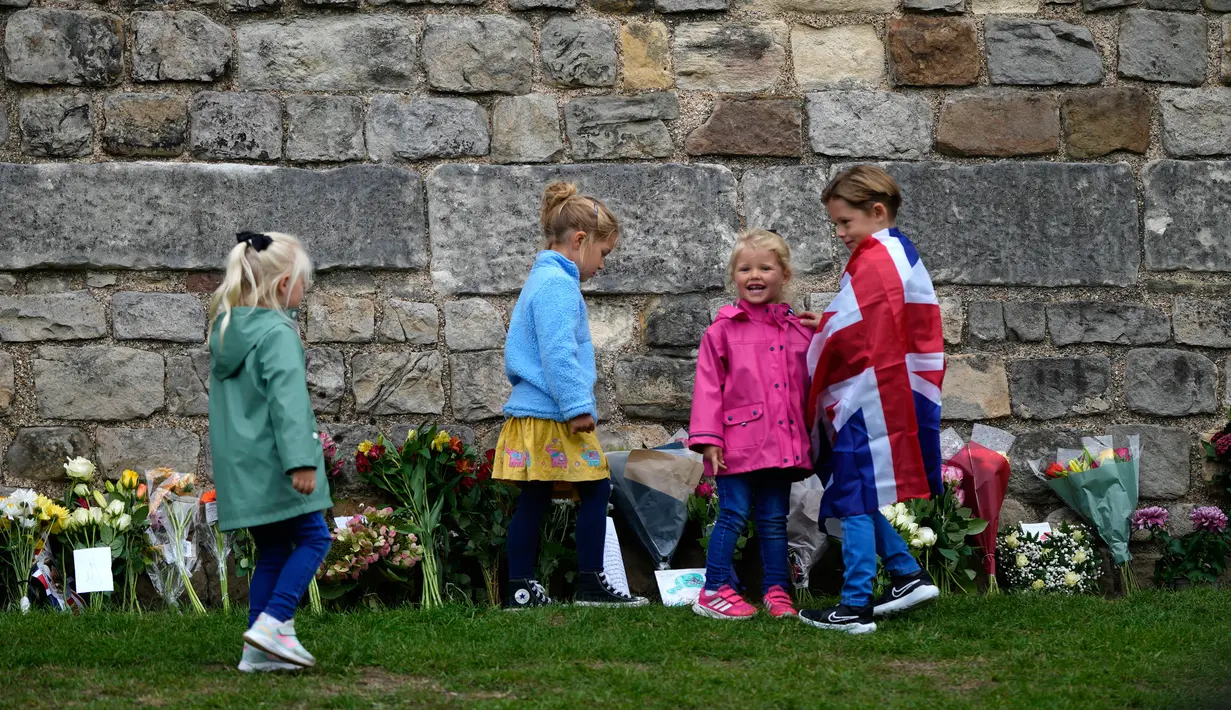 Anak-anak melihat rangkaian bunga yang ditinggalkan di luar Kastil Windsor saat mereka menunggu peti mati Ratu Elizabeth II tiba di Windsor, Inggris, Senin (19/9/2022). Prosesi pemakaman Ratu Elizabeth II yang berlangsung pada hari ini ternyata sudah sejak lama dipikirkan sang mendiang. (AP Photo/Alastair Grant, Pool)