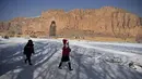 Anak-anak berjalan melalui jalan yang tertutup salju setelah turun salju dekat situs patung Buddha raksasa yang dihancurkan oleh Taliban pada 2001 di Provinsi Bamiyan, Afghanistan, 8 Januari 2021. Dahulu, daerah patung ini berdiri juga menjadi rumah untuk biara. (WAKIL KOHSAR/AFP)