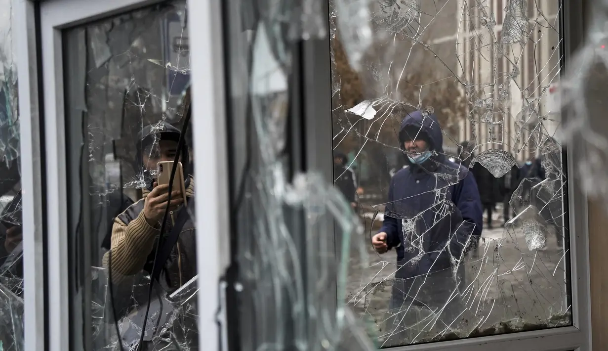 Seorang pria mengambil foto dari jendela kios polisi yang dirusak oleh demonstran selama protes di Almaty, Kazakhstan, Rabu (5/2/2022). Demonstran yang menolak kenaikan harga gas cair bentrok dengan polisi di kota terbesar Kazakhstan dan mengadakan protes di sekitar kota. (AP Photo/Vladimir Tretyako