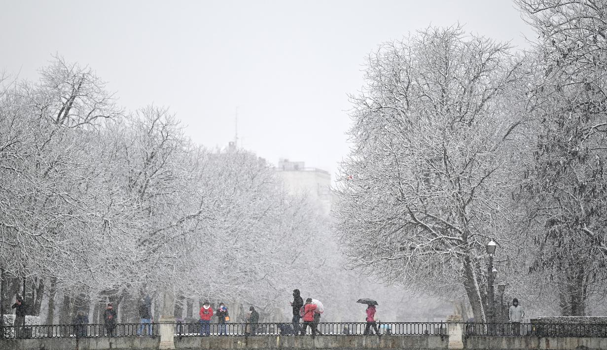 Orang-orang berjalan saat salju turun di Taman Retiro di pusat kota Madrid (7/1/2021). Sistem tekanan rendah bergerak ke timur laut dari Madeira di Atlantik, membawa massa udara yang sangat dingin ke Spanyol. (AFP/Gabriel Bouys)