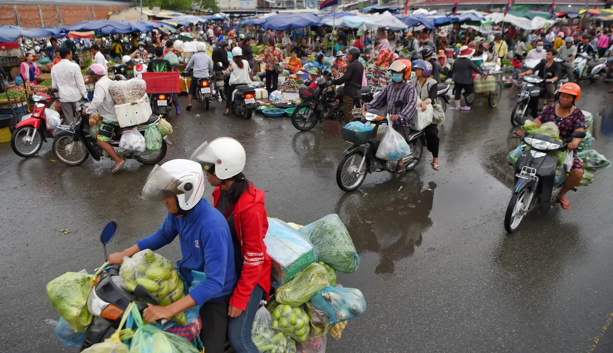 Orang-orang mengendarai sepeda motor melewati pasar di Phnom Penh (24/7/2020). Pasar membentuk bagian integral dalam kehidupan orang Kamboja, dengan kunjungan harian yang dilakukan untuk persediaan makanan untuk hari itu serta barang-barang lainnya. (AFP/Tang Chhin Sothy)