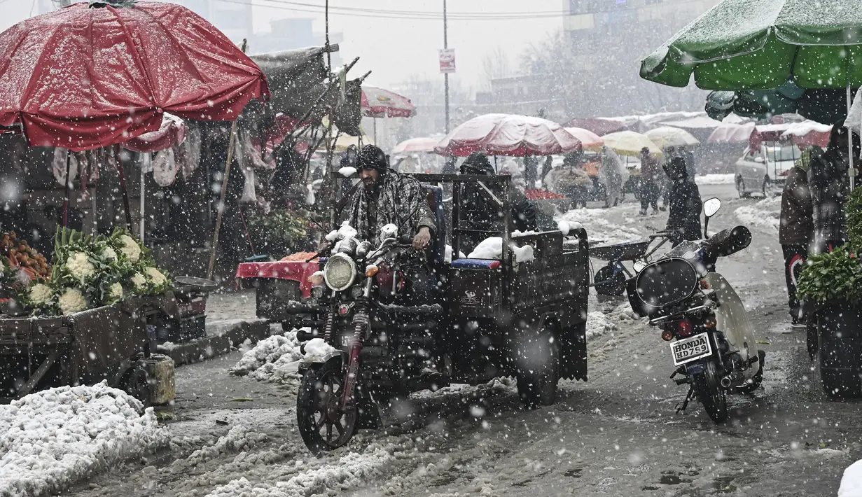 Seorang pria mengendarai kendaraan roda tiga saat hujan salju lebat di sebuah pasar di Kabul (4/1/2022). Beberapa kecelakaan terjadi pada Senin (3/1) di tengah kondisi lalu lintas yang kacau setelah hujan salju lebat. (AFP/Mohd Rasfan)