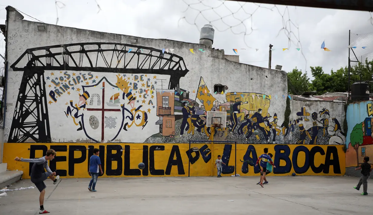 Anak-anak bermain sepak bola di taman bermain di lingkungan La Boca, ibu kota Argentina, Buenos Aires pada 27 November 2018. Kota ini dikenal sebagai markas dari Boca Juniors, tim yang pernah membesarkan Diego Maradona. (Ludovic MARIN / AFP)
