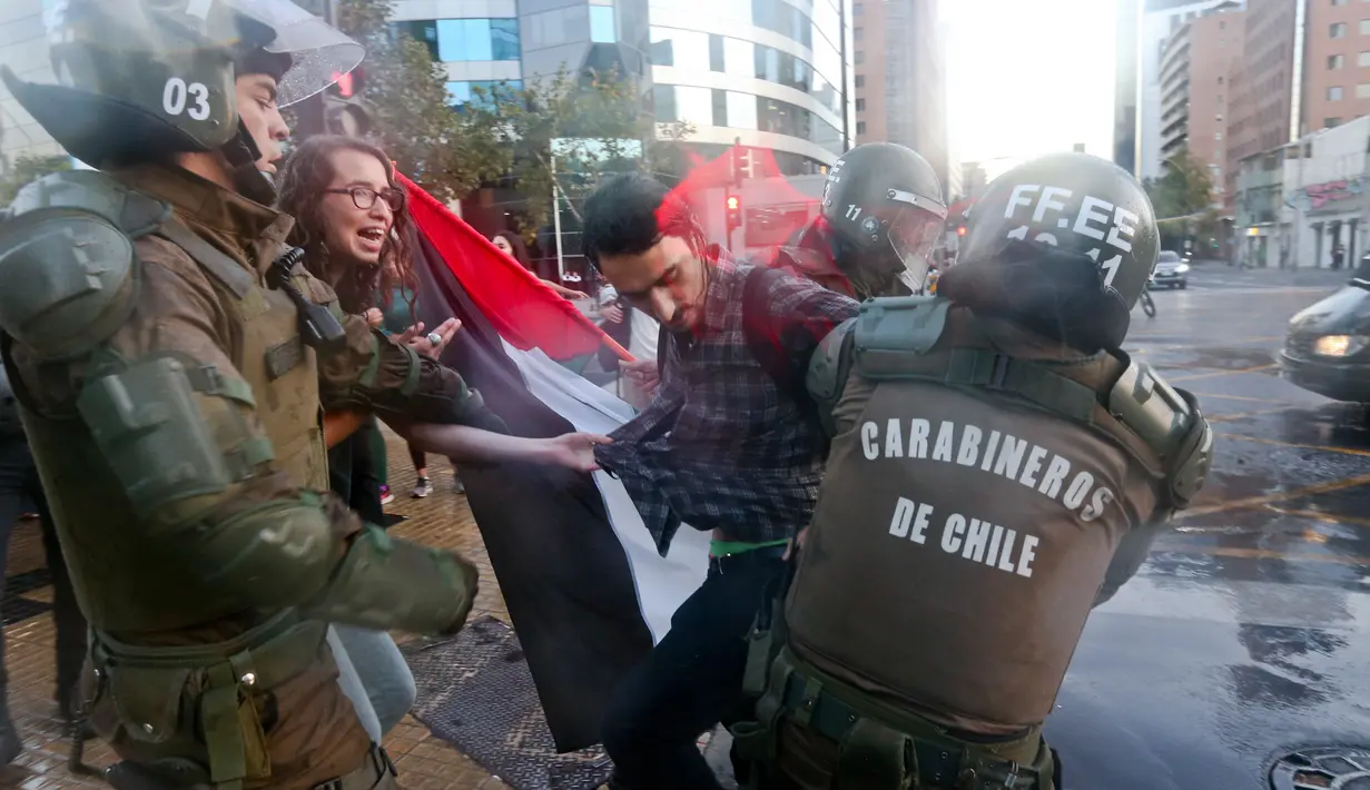 Polisi anti huru hara mengamankan seorang pengunjuk rasa saat terjadi aksi di luar kedutaan AS di Santiago, Chili (14/4). Para demonstran melakukan aksi menentang serangan AS dan sekutunya ke Suriah. (AP / Esteban Felix)