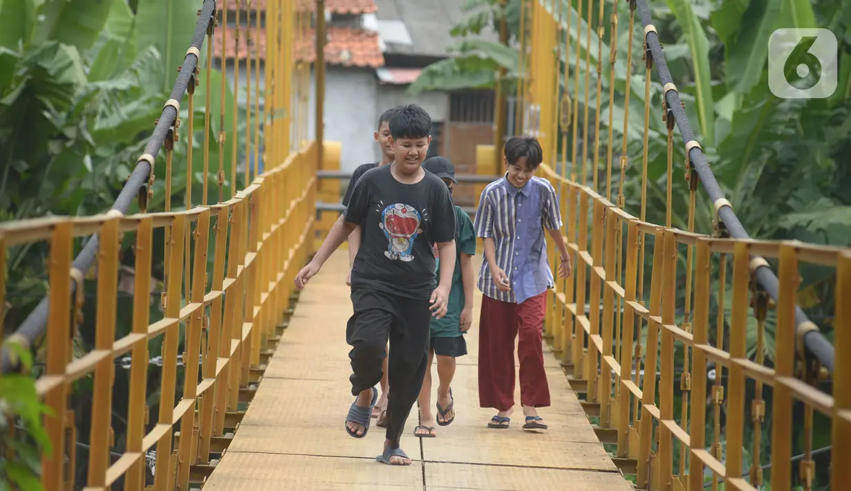 Anak-anak melintasi jembatan gantung Kuning yang menghubungkan Pasar Minggu Poltangan ke Cililitan Condet, Jakarta, Selasa (28/12/2021). Jembatan gantung Kuning dengan panjang 40 meter di atas sungai Ciliwung tersebut baru baru ini dijadikan lokasi foto untuk konten medsos. (merdeka.com/Imam Buhori)