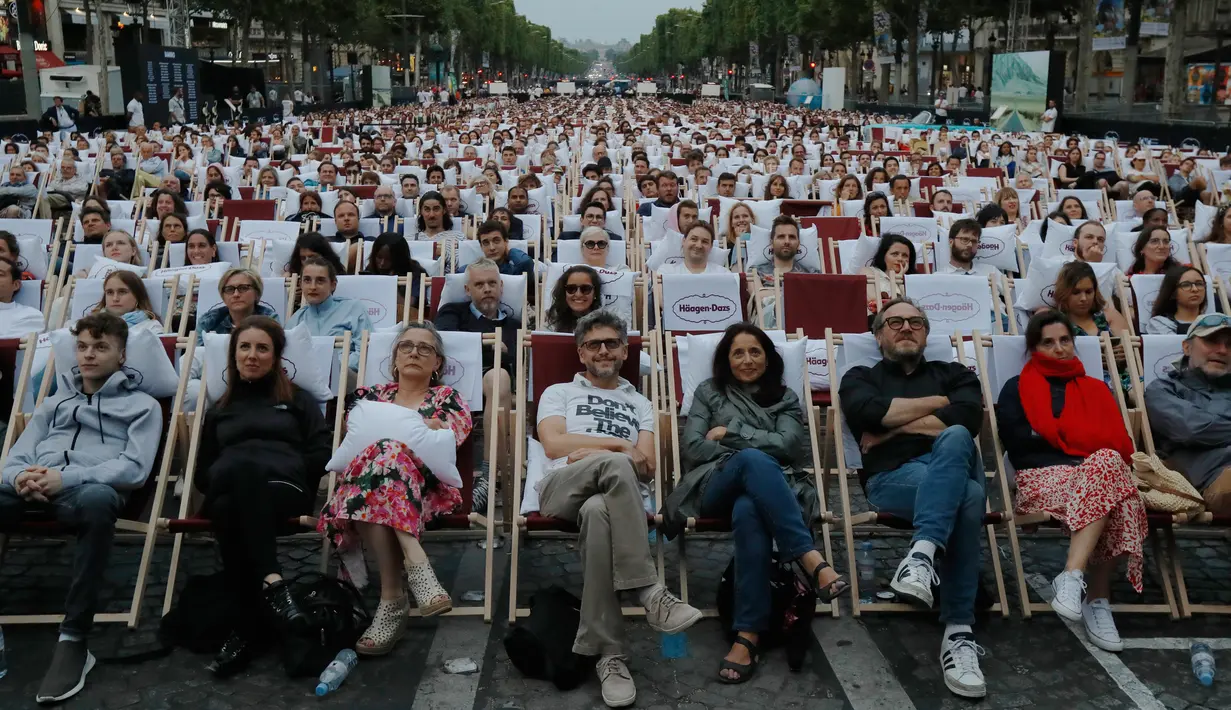 Orang-orang menonton film gratis yang diputar di ruang terbuka di jalan Champs Elysees, Paris (7/7/2019). Pemutaran bioskop luar ruangan gratis di Paris musim panas ini menayangkan film Prancis dengan teks bahasa Inggris, untuk membantu Anglophones mengikuti budaya Prancis. (AP Photo/Michel Euler)