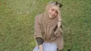 Mengenakan hijab cokelat, Cita Citata menikmati suasana di luar rumah. Duduk di rerumputan membuatnya bahagia. (Foto: Instagram/@cita_citata)