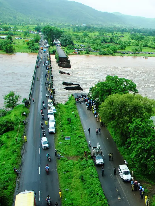 Sejumlah orang berkumpul di lokasi jembatan jalan raya yang runtuh akibat derasnya aliran sungai Savitri yang sedang meluap di barat India, Rabu (3/8). Jembatan jalan raya tersebut menghubungkan kota Mumbai dengan negara bagian Goa. (AFP)