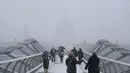 Pejalan kaki melintasi jembatan milenium dengan latar katedral St Paul saat hujan salju turun di London (27/2). (AFP Photo/Daniel Leal-Olivas)