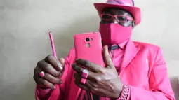 Fashionista Kenya, James Mwangi Maina bermain ponsel sambil memamerkan setelan jasnya yang senada dengan pakaian dan aksesorisnya, termasuk masker di Nairobi, 5 Agustus 2020. Mwangi memiliki lebih dari 160 jas yang warnanya serasi dengan aksesoris yang dimilikinya. (Simon MAINA/AFP)
