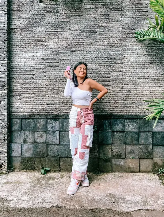 Celana cargo hadir dengan ragam motif seperti tambal sulam dengan warna yang cute. Awkarin memasangkannya dengan atasan putih one shoulder. (Foto: Instagram Awkarin)