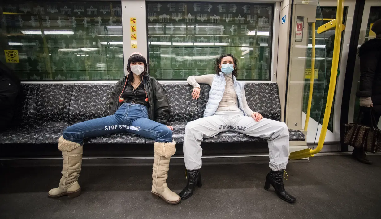 Elena Buscaino (kanan) dan Mina Bonakdar berpose dengan Riot Pants bertuliskan "Stop Spreading" di kereta bawah tanah di Berlin, 5 Februari 2021. Aktivis feminis itu dalam misi menghentikan kebiasaan penumpang pria melebarkan kaki saat duduk sehingga memakan dua kursi kereta. (STEFANIE LOOS/AFP)