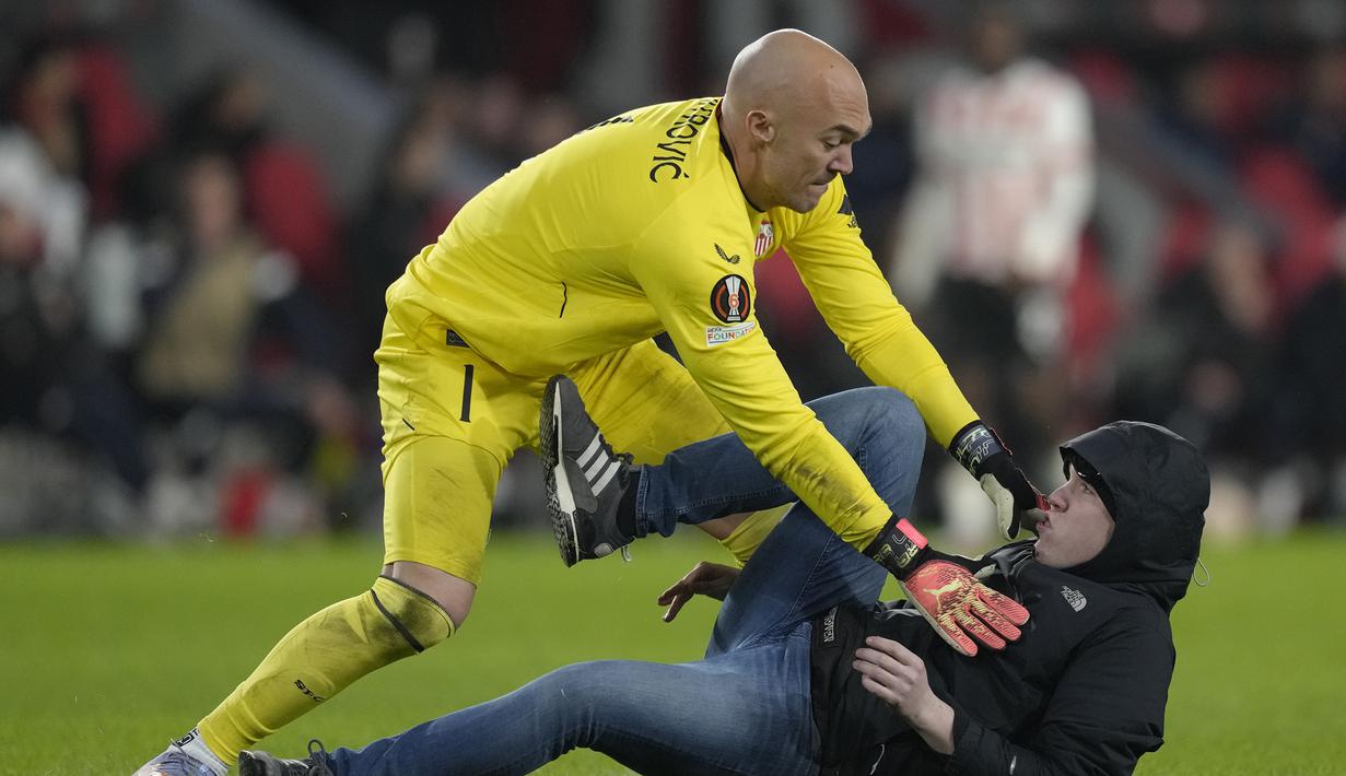 Kiper Sevilla, Marko Dmitrovic tengah viral di jagat maya setelah laga menghadapi PSV dalam babak playoff fase gugur Liga Europa 2022/2023, Jumat (24/2/2023) dini hari WIB. Bukan aksinya dalam menjaga gawangnya dari ancaman para pemain PSV, namun aksinya saat melumpuhkan suporter fanatik alias hooligan tuan rumah lah yang membuatnya kini jadi perhatian dunia. Mau lihat aksinya? Ini dia! (AP Photo/Peter Dejong)