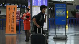 Seorang penumpang mendorong barang bawaannya melewati staf pesawat yang berdiri di dekat konter check-in yang sepi di Bandara Internasional Pudong, Shanghai, Minggu (25/7/2021). Ratusan jadwal penerbangan dibatalkan saat topan In-Fa bergerak menuju mendarat. (AP Photo/Andy Wong)