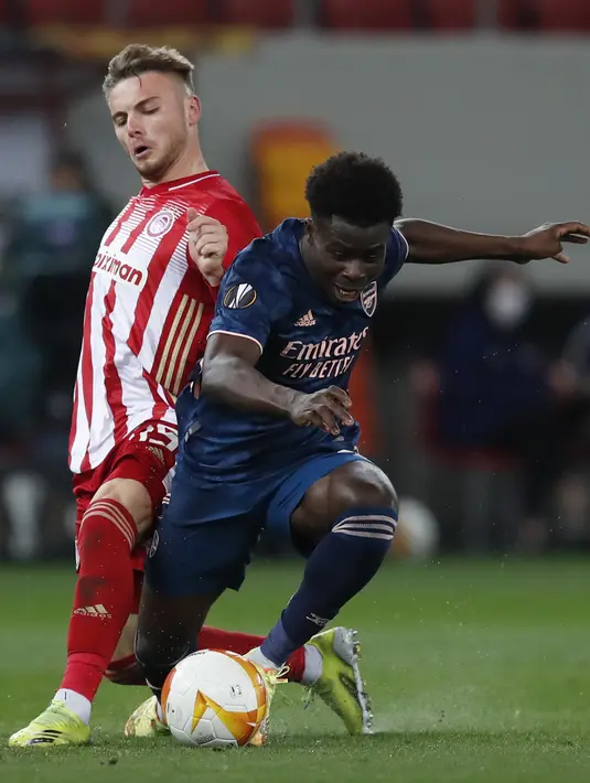 Gelandang Arsenal, Bukayo Saka berebut bola dengan gelandang Olympiakos, Andreas Bouchalakis pada pertandingan leg pertama babak 16 besar Liga Europa di stadion Georgios Karaiskakis, Athena, Jumat (12/3/2021). Arsenal menang atas Olympiakos 3-1. (AP Photo/Thanassis Stavrakis)