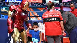 Seorang anak laki-laki berpose di samping seseorang berkostum superhero Ironman sebelum menerima vaksin Covid-19 Pfizer-BioNtech untuk anak-anak berusia 5-11 di sebuah gym di San Juan City, pinggiran kota Manila, Filipina pada 7 Februari 2022. (Ted ALJIBE / AFP)