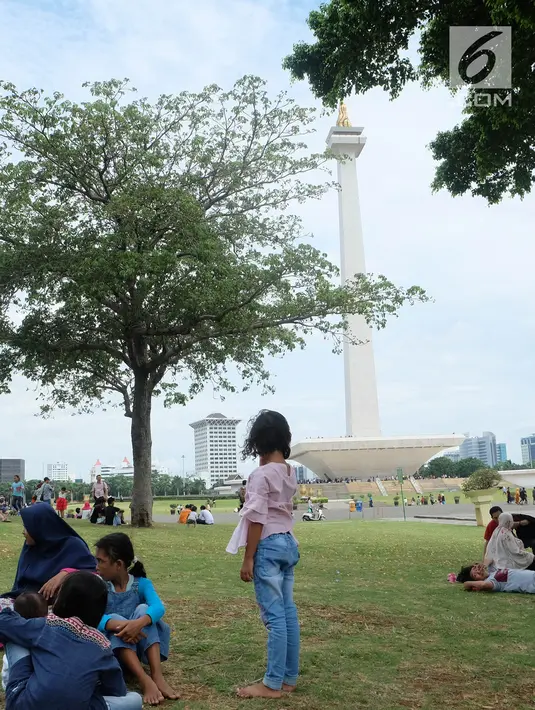 Sejumlah pengunjung beristirahat di rumput selama liburan di Monumen Nasional (monas), Jakarta, Selasa (25/12). Liburan Natal 2018, banyak warga datang bersama kerabat maupun keluarga memadati Monas. (Liputan6.com/Herman Zakharia)