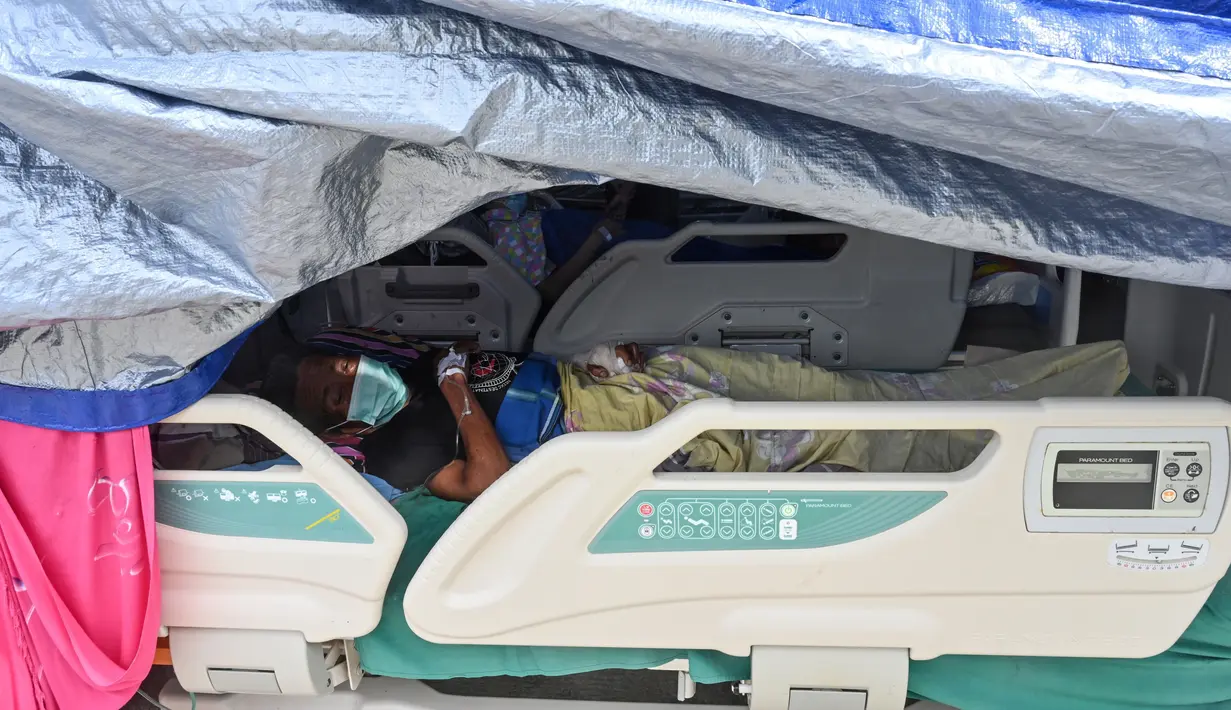Seorang pria yang terluka dalam gempa dengan magnitudo 6,2 beristirahat di tempat penampungan sementara di luar Rumah Sakit Regional Sulbar, Mamuju, Sulawesi Barat, Minggu (17/1/2021). Mereka dirawat di dalam tenda darurat untuk mengantisipasi gempa susulan. (ADEK BERRY/AFP)