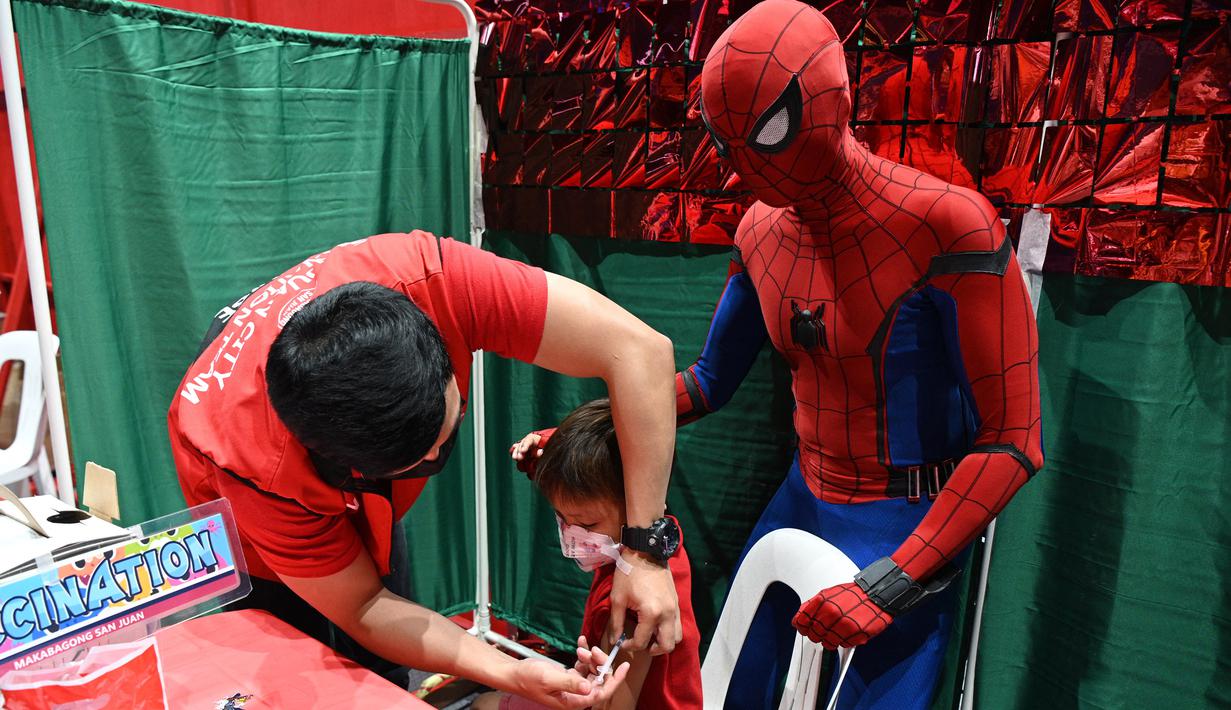 Seorang anak menerima vaksin Covid-19 Pfizer-BioNtech untuk anak-anak berusia 5-11 tahun saat seseorang berkostum superhero Spider-Man terlihat di gym di San Juan City, pinggiran kota Manila, Filipina pada 7 Februari 2022. (Ted ALJIBE / AFP)