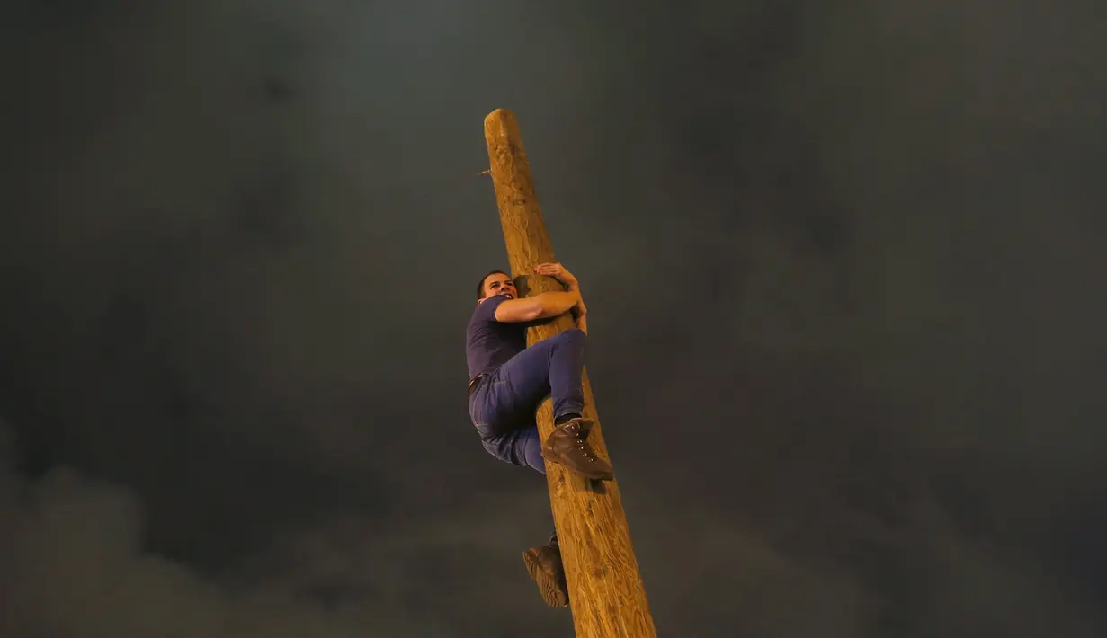 Seorang pria memanjat tiang kayu selama perayaan Maslenitsa di kota Krasnoyarsk, Rusia, (13/3). Mereka rela menaiki tiyang setinggi 9 meter tanpa bantuan alat apapun untuk mendapatkan hadiah. (REUTERS / Ilya Naymushin)
