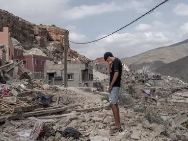 Seorang pemuda berdiri di atas reruntuhan rumah yang hancur di tengah operasi penyelamatan yang sedang berlangsung di desa Imi N'Tala, dekat Amizmiz, pada tanggal 12 September 2023. (BULENT KILIC/AFP)