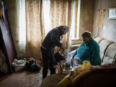 Lyubov Lomachuk (69) menyajikan teh untuk tetangganya Valentyna Volynets (59) setelah merebus air di api darurat di taman umum dekat gedung mereka di Bucha, Kiev, Senin (18/4/2022). Warga Bucha masih tanpa listrik, air dan gas setelah lebih dari 43 hari sejak invasi Rusia (AP Photo/Emilio Morenatti)