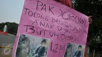 Susanto (28) memegang kertas  bertulisan: “ Pak Jokowi tolong beli ginjal saya, anak saya butuh operasi 1,2 milyar”, saat melakukan aksinya di depan Istana Merdeka, Jakarta, Jumat (20/11). (Liputan6.com/Gempur M Surya)
