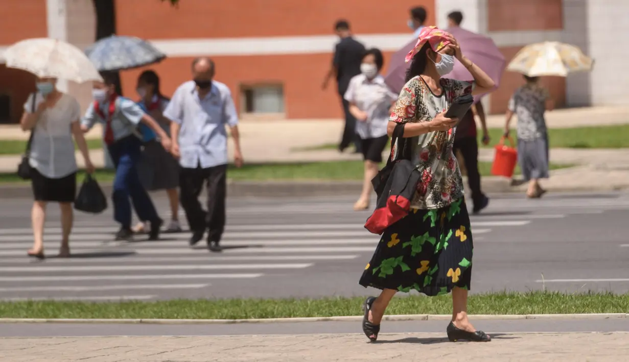 Pejalan kaki menyeberang jalan saat suhu tinggi mencapai 34 derajat celsius di Pyongyang, Korea Utara, Rabu (21/7/2021). Musim Panas dimulai pada bulan Juni hingga Agustus, dan puncak musim panas adalah bulan Agustus. (KIM Won Jin / AFP)